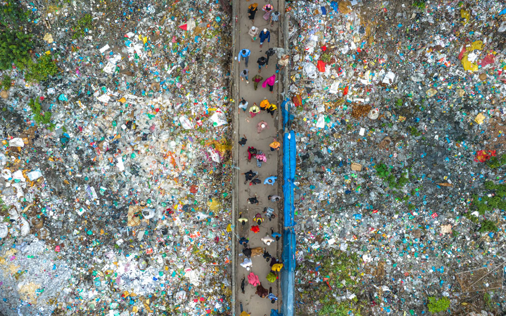 Camminata attraverso la spazzatura, persone su un ponte sospeso su un fiume di spazzatura di plastica